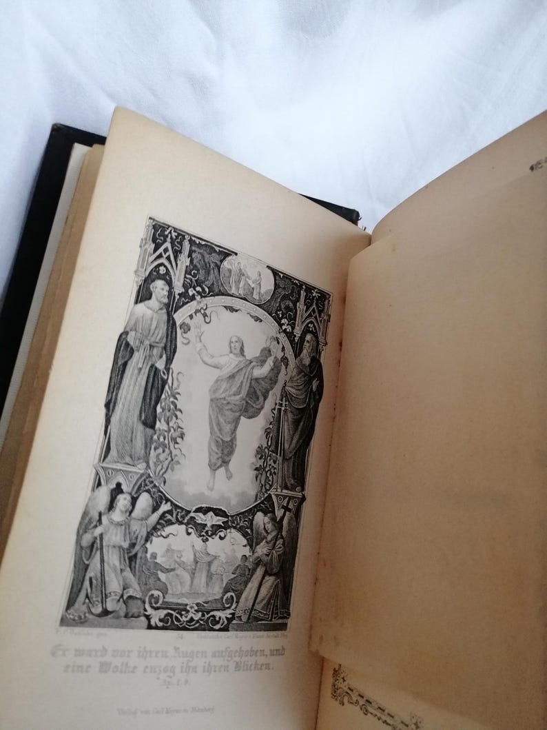 May include: An open antique book with a black spine, displaying a detailed black and white illustration. The illustration depicts figures in religious attire, with text in German below the image. The pages are aged with a yellowed hue.