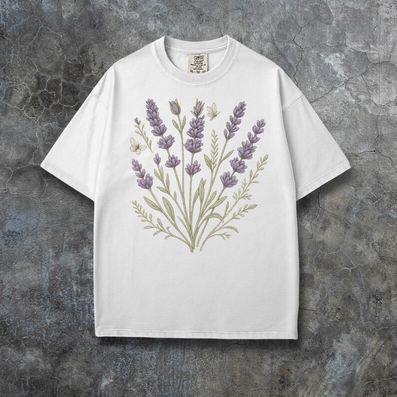 Puede incluir: Camiseta blanca con un dise&ntilde;o floral de lavanda y mariposas. El gr&aacute;fico incluye ramitas de lavanda en tonos morados y verdes. La camiseta tiene cuello redondo y mangas cortas. La etiqueta de la camiseta dice "COMIC COLORS".