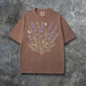 Puede incluir: Camiseta marr&oacute;n con un dise&ntilde;o de lavanda y mariposas. El gr&aacute;fico incluye ramitas de lavanda en tonos morados y verdes, con dos mariposas blancas. La camiseta tiene cuello redondo y mangas cortas. La etiqueta dice "Comfort Colors".