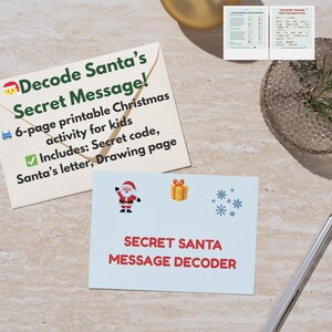 Può includere: Una carta azzurra con la scritta "SECRET SANTA MESSAGE DECODER" e un'illustrazione di Babbo Natale. È visibile anche una busta con la scritta "Decode Santa's Secret Message!". L'immagine include una penna e un elemento decorativo.