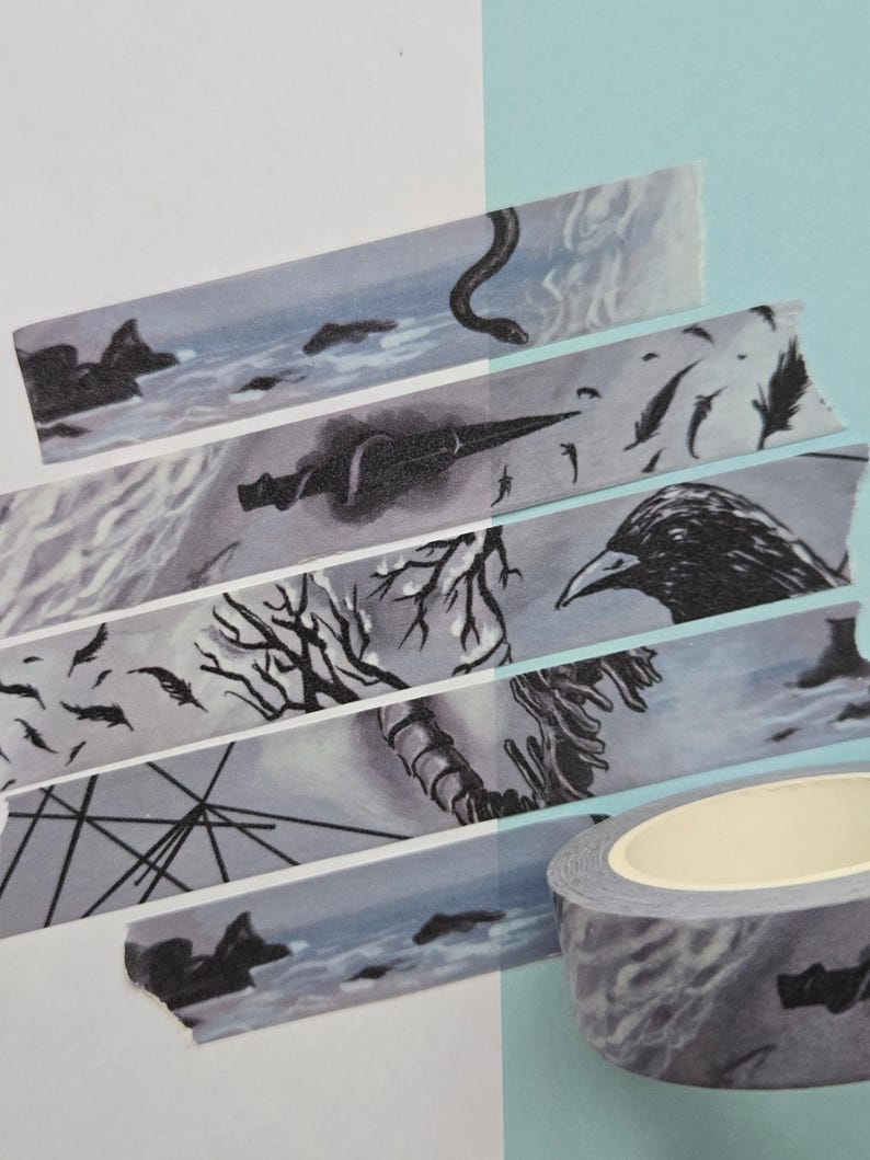 May include: Decorative washi tape roll with a gray and white design. The tape features illustrations of a snake, crow, feathers, and a seascape. The tape is partially unrolled, revealing the design. The background is white and light blue.