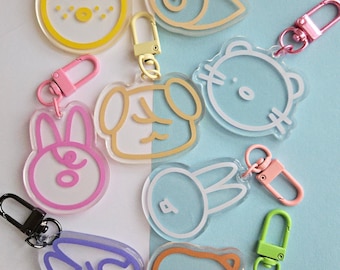 May include: A collection of clear acrylic keychains with colorful outlines and hardware. The keychains feature various animal and abstract designs in shades of yellow, pink, orange, purple, and blue. Each keychain has a metal clasp.