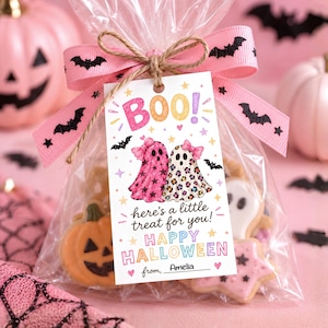 May include: A clear plastic treat bag filled with Halloween cookies, tied with a pink ribbon featuring black bats. A rectangular gift tag is attached, displaying two ghosts with pink bows, the text BOO!, here's a little treat for you!, HAPPY HALLOWEEN, and from, Amelia.