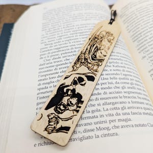 Peut inclure: Marque-page en bois avec une illustration gravée d'un guerrier fantastique et d'un monstre. Le marque-page est rectangulaire avec un cordon noir. L'œuvre est en noir sur le bois clair.