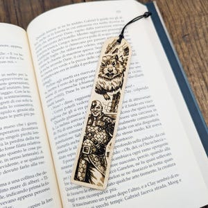 May include: Wooden bookmark with a laser-etched design. Features a detailed illustration of a cartoonish rodent and a bald, muscular character. Includes a black cord for easy placement in a book.
