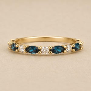 Puede incluir: Un anillo de oro con piedras preciosas azules en forma de marquesa alternadas con piedras redondas y claras. El anillo tiene un diseño delicado con pequeñas cuentas de oro entre cada piedra, creando un patrón continuo.