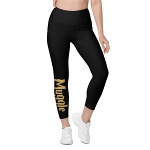 Puede incluir: Leggings negros con cintura alta y bolsillo lateral. La palabra "Muggle" está impresa verticalmente en letras doradas en la pierna izquierda. Los leggings están hechos de un material elástico.