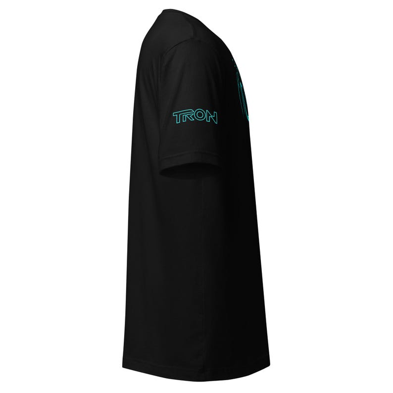 May include: Black t-shirt with the word "TRON" in teal on the left sleeve. A teal graphic is visible on the upper back of the shirt. The shirt is made of a soft material.