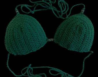 May include: A dark green, handmade crochet bikini top. The top features two triangular cups connected by a small band. The straps are long and made of the same yarn, designed to tie around the neck and back. The background is black.