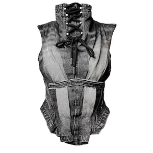 May include: A sleeveless denim corset in shades of gray. The corset features a high, laced collar and a cinched waist. Black lacing and silver-toned eyelets detail the front. The garment has a structured, form-fitting design.