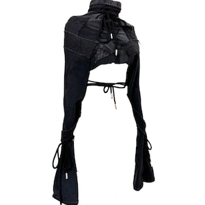 May include: A black denim bolero jacket with a high collar and long sleeves. The jacket features a patchwork design on the upper portion and ties at the waist and wrists. The sleeves are flared at the ends.