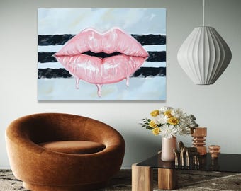 May include: A large canvas art piece featuring a close-up of glossy, pink lips with dripping gloss. The background has black and white stripes over a light blue and white backdrop. The artwork is displayed in a modern living room setting.
