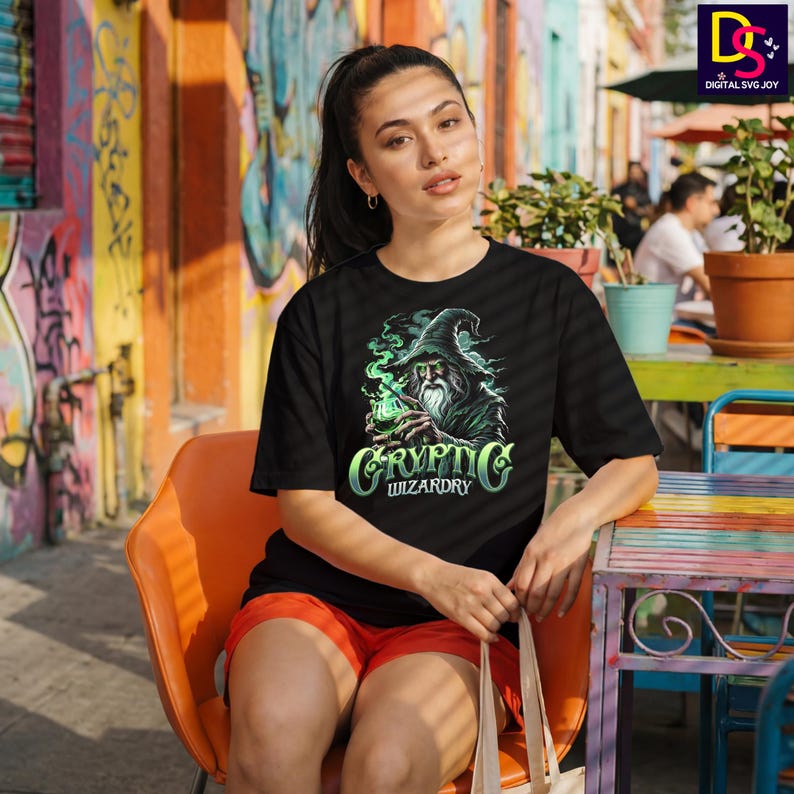 May include: Black t-shirt featuring a wizard graphic with the text "Cryptic Wizardry" in a stylized font. The wizard is depicted with a long beard and a pointed hat, surrounded by green smoke. The shirt is worn by a person sitting outdoors.