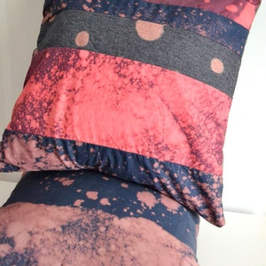 May include: Two decorative throw pillows with a patchwork design. The pillows are made of different fabrics with a splatter paint effect in shades of pink, red, blue, and gray.