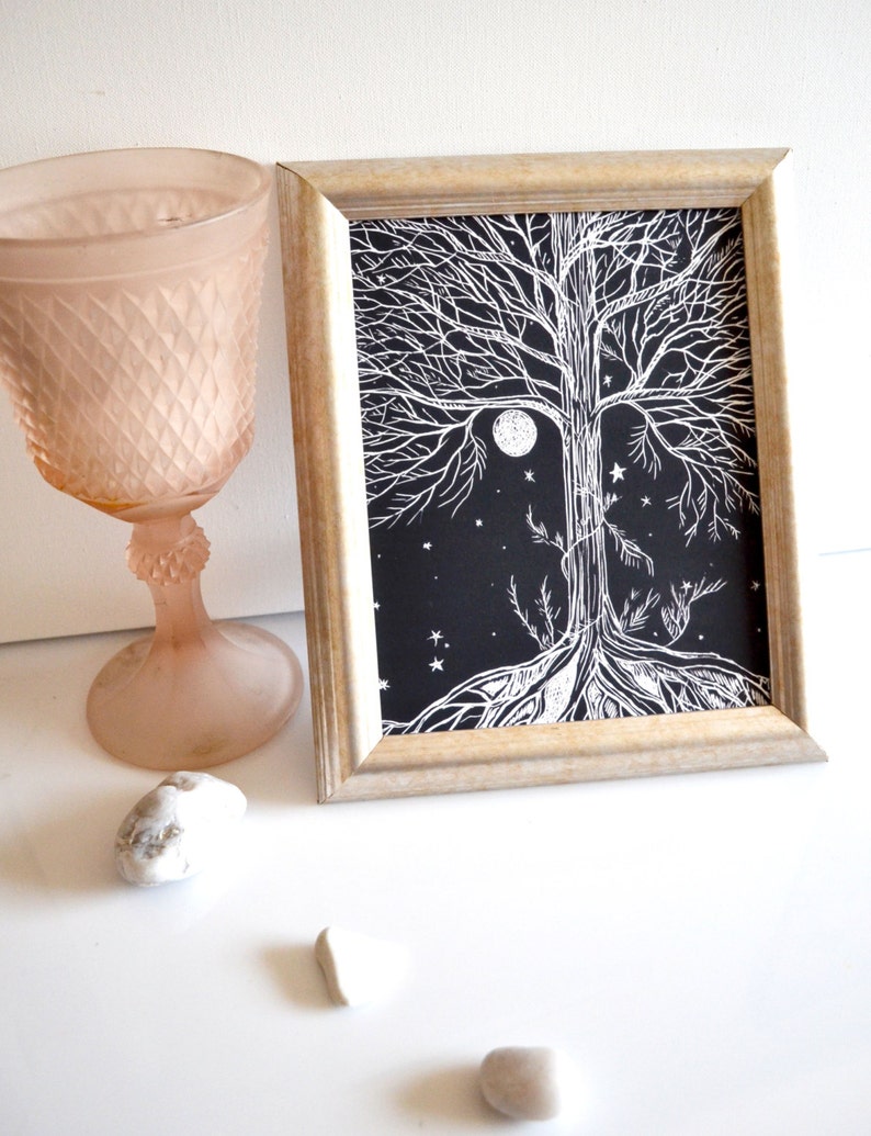 Puede incluir: Una impresi&oacute;n enmarcada en blanco y negro de un &aacute;rbol con ra&iacute;ces y ramas que se extienden hasta los bordes del papel. El &aacute;rbol est&aacute; rodeado de una luna llena y estrellas. La impresi&oacute;n est&aacute; en un marco de madera claro.