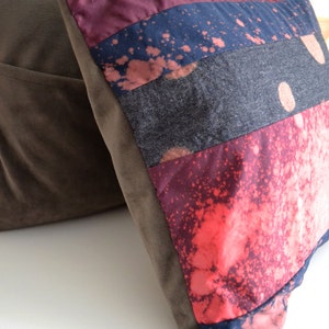 May include: A multi-colored throw pillow with a patchwork design. The pillow is made of different fabrics, including denim, velvet, and cotton. The pillow has a splatter paint design in shades of pink, blue, and white.