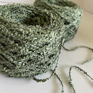 May include: Two skeins of green yarn, one partially unwound, with a textured, fuzzy appearance.