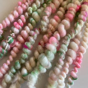 Puede incluir: Primer plano de un ovillo de hilo de color rosa, verde y blanco. El hilo es suave y esponjoso, perfecto para tejer o hacer ganchillo.