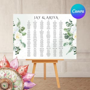 Könnte beinhalten: Eine weiße Hochzeits-Sitzordnung mit Gästenamen, floralen Akzenten und den Namen "JAY & ARIYA". Die Tafel wird auf einer hölzernen Staffelei präsentiert.
