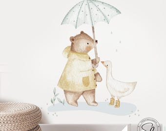 Puede incluir: Ilustración en acuarela de un oso con impermeable amarillo sosteniendo un paraguas celeste con lunares blancos, protegiendo a un ganso blanco con botas amarillas. Caída de gotas de lluvia. Calcomanía de pared.