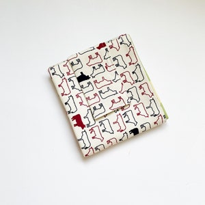 May include: A white fabric pouch with a black and red cow print design. The pouch is folded in half and the print is visible on both sides.