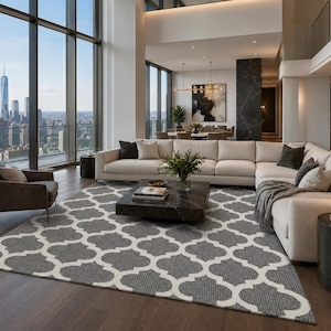 May include: A rectangular area rug featuring a repeating quatrefoil pattern in dark grey and off-white. The rug has a textured, woven surface and is positioned on a dark wood floor, extending from beneath a low black coffee table to the seating area.