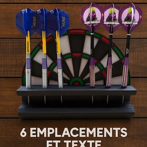 Puede incluir: Un conjunto de dardos con plumas azules y moradas, cañas amarillas y barriles plateados, colocados en un soporte negro frente a una diana. La imagen incluye el texto "6 EMPLACEMENTS ET TEXTE PERSONNALISABLE".