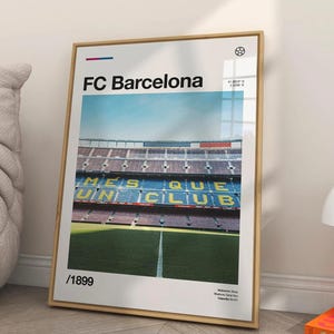 May include: A framed poster featuring the FC Barcelona stadium. The poster has a gold frame and displays the stadium's interior with green field and blue seating. The text "FC Barcelona" and "/1899" are visible.