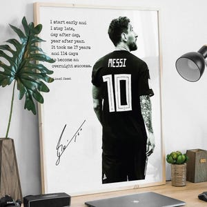 May include: A framed print featuring a black and white image of a soccer player wearing a black jersey with the number 10 and the name MESSI. The print includes a quote about hard work. The print is on a wooden desk.