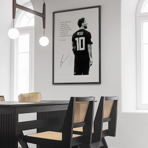 May include: Framed black and white print featuring a soccer player in a black jersey with the number 10 and the name MESSI. The print includes a quote and a signature. The print is displayed on a white wall.