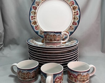 Puede incluir: Un juego de vajilla que incluye una pila de platos redondos y cuatro tazas. Cada pieza es blanca con un borde azul oscuro decorado con una colorida escena de pueblo invernal y un patrón de cuadros rojos y blancos en la base de las tazas.