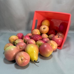 May include: A bright coral plastic bin tipped on its side, spilling a collection of artificial fruit. The assortment includes various round apples and a single pear, all featuring a gradient of yellow, pink, and red colors with smooth surfaces.