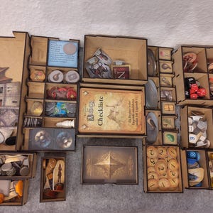 Könnte beinhalten: Holz-Spiel-Organizer mit mehreren Fächern, gefüllt mit Spielsteinen, Karten und Würfeln. Der Organizer enthält verschiedene Spielsteine, Figuren und eine Karte mit der Aufschrift "ANDOR Checklist". Das Farbschema ist braun und beige.