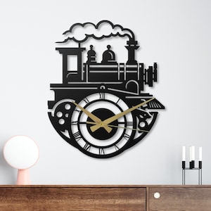 May include: Black metal wall clock in the shape of a vintage steam train. The clock features Roman numerals and gold-colored clock hands. The train design includes details like a smokestack and a cloud of smoke.