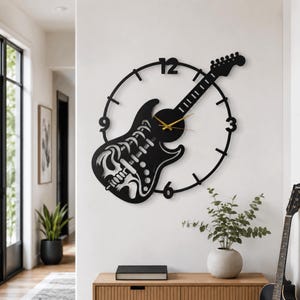 Könnte beinhalten: Eine schwarze Wanduhr in Form einer E-Gitarre mit einem in den Korpus integrierten Skelett-Brustkorb-Design. Die Uhr verfügt über einen kreisförmigen Rahmen mit den Ziffern 3, 6, 9 und 12 sowie dünne goldfarbene Zeiger in der Mitte des Korpus.