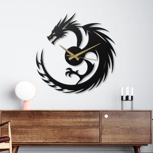 May include: A black metal dragon wall clock with gold-colored hands. The dragon design is stylized with sharp edges and a circular tail. The clock is mounted on a white wall above a wooden cabinet.