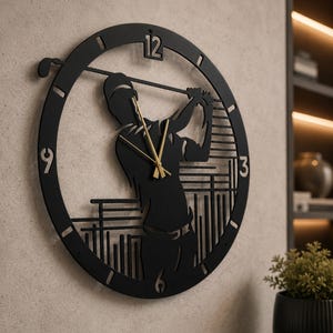 Può includere: Un orologio da parete circolare nero con la sagoma ritagliata di un golfista durante lo swing. Il quadrante include i numeri 3, 6, 9 e 12, con sottili lancette dorate per ore, minuti e secondi posizionate al centro del busto del golfista.