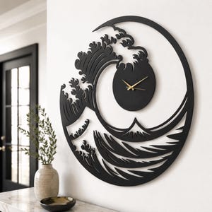 May include: A circular wall clock featuring a black cutout design of a stylized ocean wave and a mountain peak. The clock face is a solid black circle integrated into the wave pattern, equipped with thin gold-colored hour, minute, and second hands.