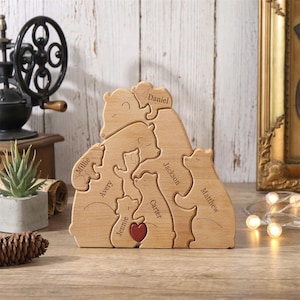 Peut inclure: Puzzle familial en bois repr&eacute;sentant des ours. Chaque ours est grav&eacute; d'un nom, avec un c&oelig;ur rouge au centre. Le puzzle est en bois clair et est pr&eacute;sent&eacute; sur une surface en bois.