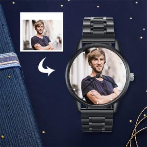 May include: Black wristwatch featuring a photograph of a person on the watch face. The watch has a black metal strap and a round face with small, white markers. A smaller photo of the same person is in the upper left corner. The background is dark blue with gold stars.