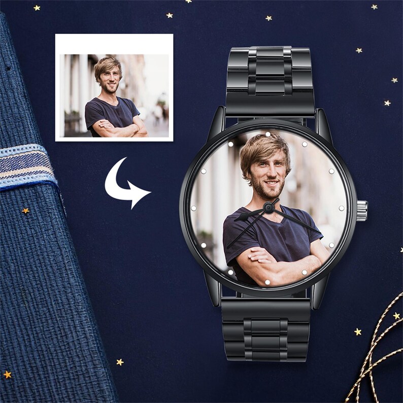 May include: Black wristwatch featuring a photograph of a person on the watch face. The watch has a black metal strap and a round face with small, white markers. A smaller photo of the same person is in the upper left corner. The background is dark blue with gold stars.
