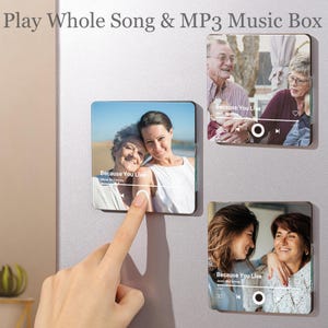 May include: Square MP3 music box with family photos. The text "Play Whole Song & MP3 Music Box" is at the top. The music box displays a song interface with the text "Because You Live". A finger touches the screen.