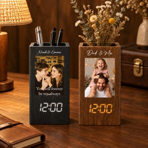 Könnte beinhalten: Zwei rechteckige Schreibtisch-Organizer aus Holz mit integrierten Digitaluhren. Der schwarze Organizer zeigt ein Foto eines Paares mit dem Text Noah & Emma und You will forever be my always. Der braune Organizer zeigt ein Foto eines Kindes und eines Elternteils mit dem Text Dad & Me.