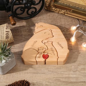 Peut inclure: Puzzle familial en bois repr&eacute;sentant des ours, avec les noms "Lucilla", "Matthew", "Jackson" et "Millie" grav&eacute;s. Un c&oelig;ur rouge est plac&eacute; entre les deux petits ours. Le puzzle est en bois clair.