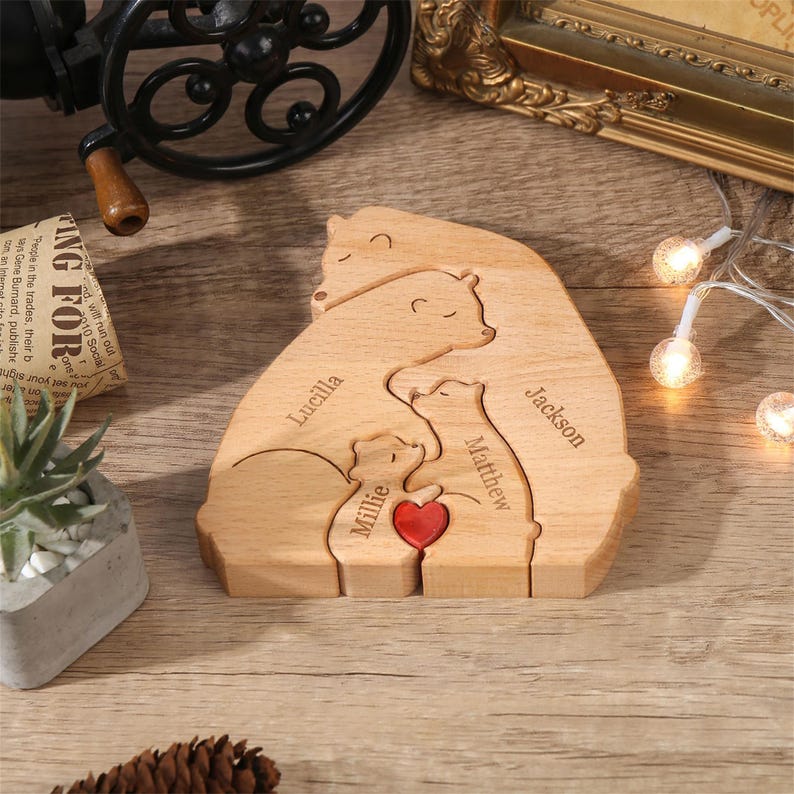 Peut inclure: Puzzle familial en bois repr&eacute;sentant des ours, avec les noms "Lucilla", "Matthew", "Jackson" et "Millie" grav&eacute;s. Un c&oelig;ur rouge est plac&eacute; entre les deux petits ours. Le puzzle est en bois clair.