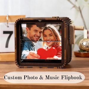 May include: A dark brown wooden flipbook featuring a photo of a couple holding a red heart. It has a crank on the side. The text "Custom Photo & Music Flipbook" is at the bottom.