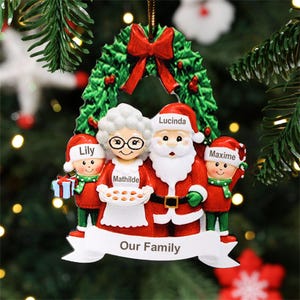 May include: A festive Christmas tree ornament depicting a family dressed as Santa Claus and Mrs. Claus. The ornament includes a green wreath with a red bow, and the words "Our Family". The names Lily, Mathilde, Lucinda, and Maxime are displayed on the ornament.