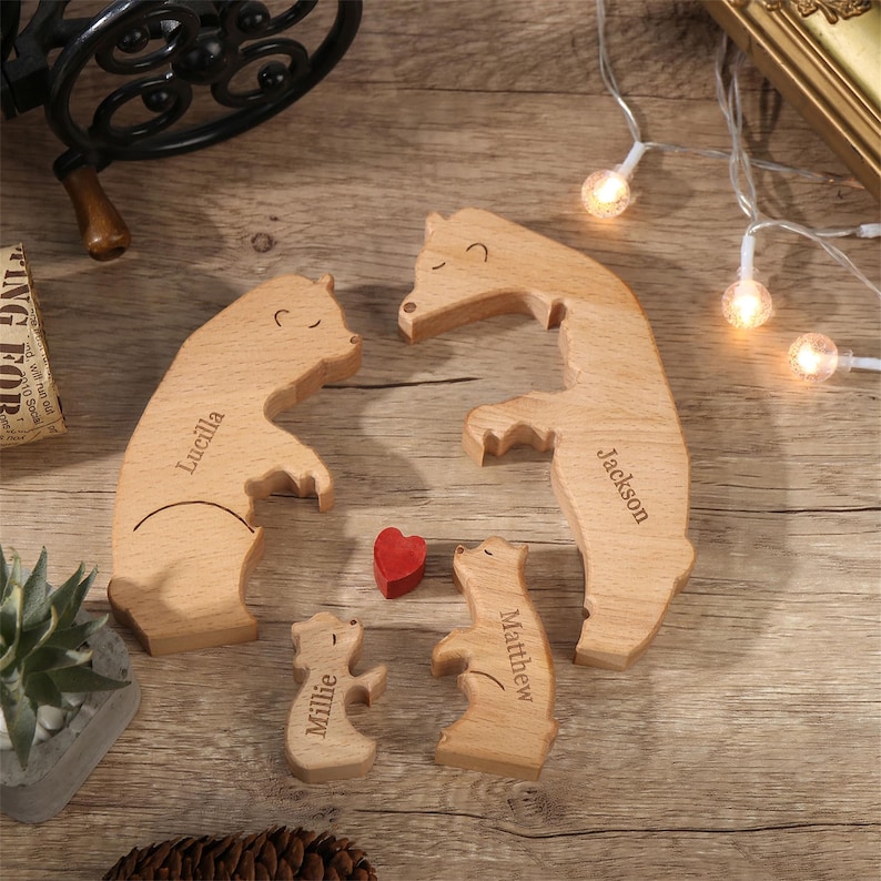 Peut inclure: Figurines en bois repr&eacute;sentant une famille d'ours avec les noms grav&eacute;s : Lucilla, Jackson, Millie et Matthew. Un petit c&oelig;ur rouge est plac&eacute; entre les ours. Les ours sont en bois clair, dispos&eacute;s sur une surface en bois.