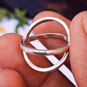 May include: A silver ring with a distinctive double-band design. The ring showcases two interconnected, circular bands, offering a modern and minimalist aesthetic. The polished metal reflects light, emphasising the ring's smooth surface and simple elegance.