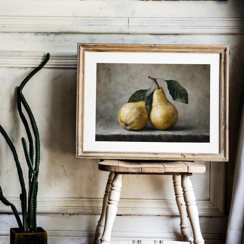 May include: A framed art print featuring a still life painting of two yellow pears with green leaves. The pears are positioned on a dark surface against a neutral, textured background. The artwork is enclosed in a light-colored wooden frame.